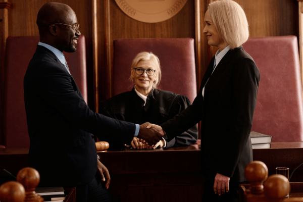 Two attorneys shaking hands in courtroom discussing is a defense attorney the same as a lawyer