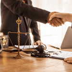 Lawyer and defense attorney shaking hands across desk with scales of justice and gavel representing legal representation differences
