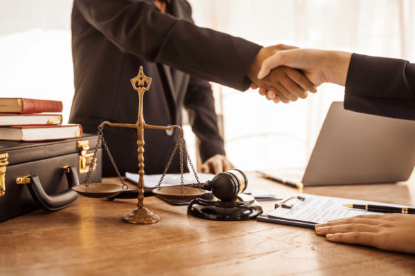 Lawyer and defense attorney shaking hands across desk with scales of justice and gavel representing legal representation differences