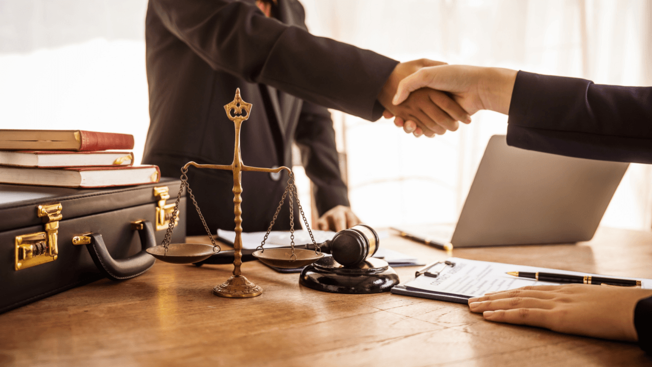 Lawyer and defense attorney shaking hands across desk with scales of justice and gavel representing legal representation differences
