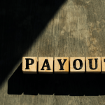 Wooden letter blocks spelling PAYOUTS on a rustic surface