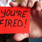 Person holding a red card that reads "You're Fired"