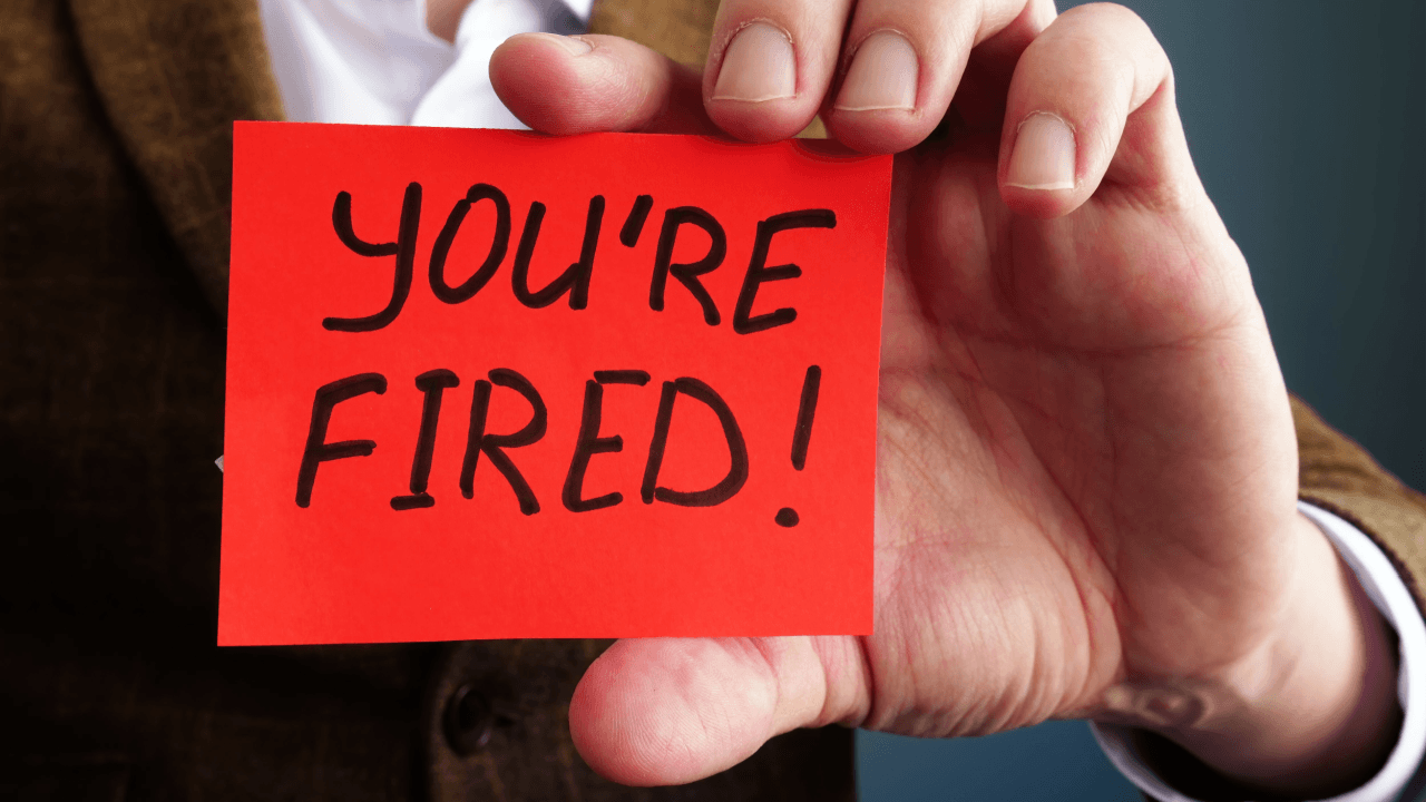 Person holding a red card that reads "You're Fired"