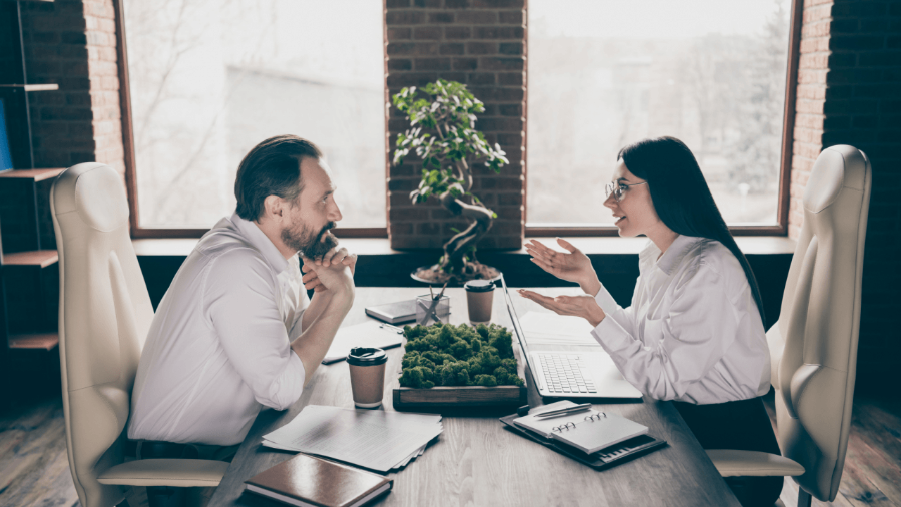Two professionals having a serious conversation across an office desk