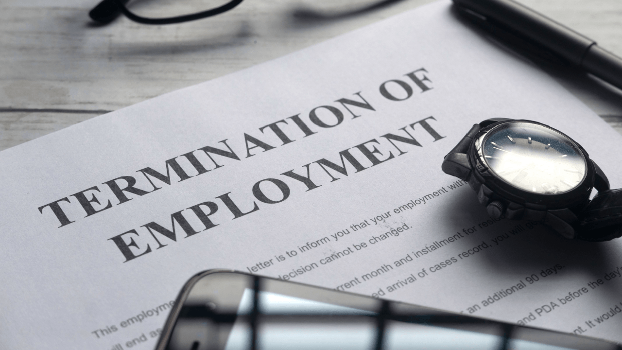 Termination of employment letter on a desk with a watch, phone, glasses, and pen