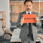Professional holding No Racism sign in office standing against race discrimination at work