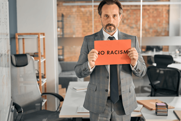 Professional holding No Racism sign in office standing against race discrimination at work