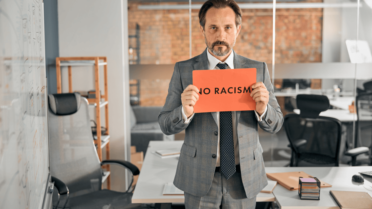 Professional holding No Racism sign in office standing against race discrimination at work