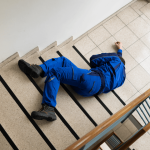 Worker in blue uniform lying on tiled landing after a slip and fall on stairs