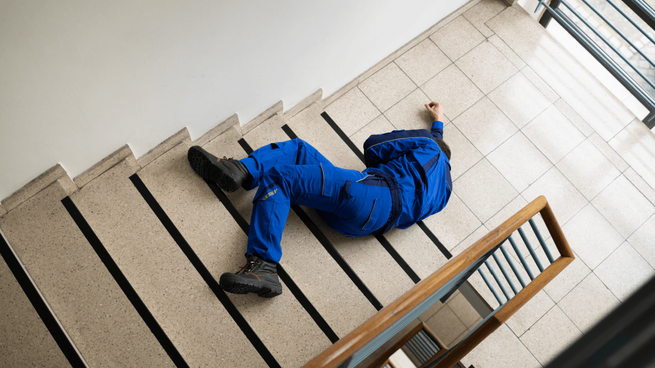 Worker in blue uniform lying on tiled landing after a slip and fall on stairs