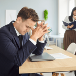 Stressed employee at desk understanding workplace bullying vs harassment from coworkers pointing behind him