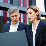 Workplace harassment lawyer consulting with colleague over laptop outside corporate building