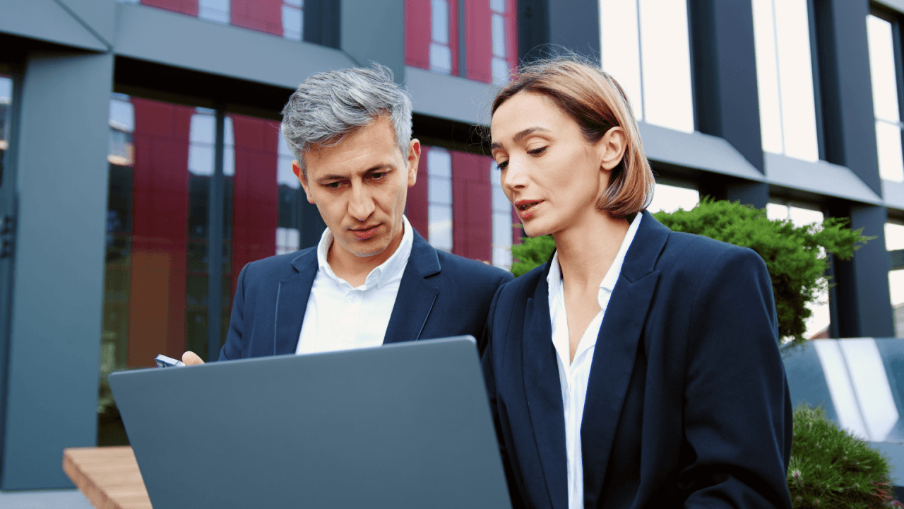 Workplace harassment lawyer consulting with colleague over laptop outside corporate building